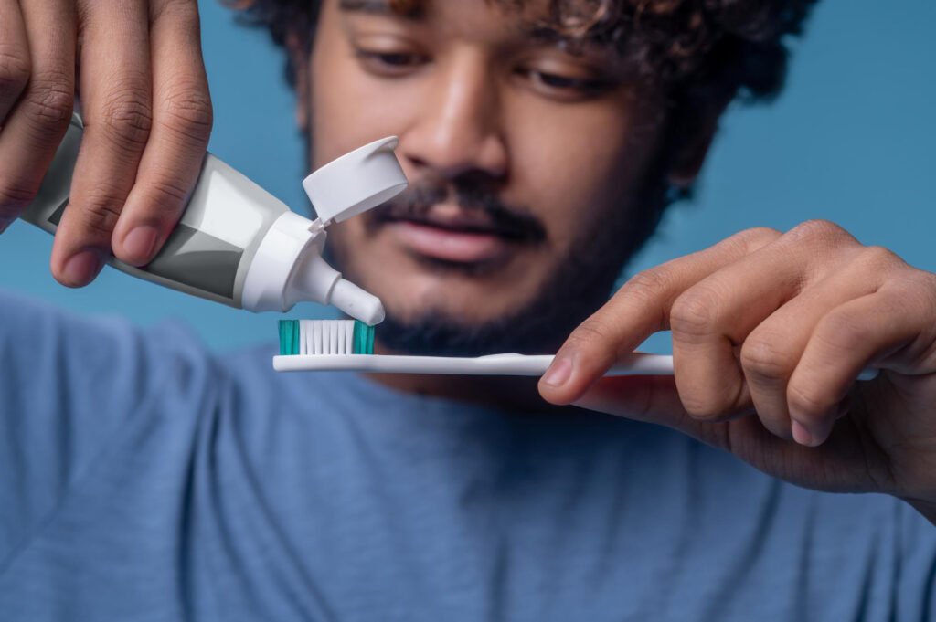 focused indian male squeezing out toothpaste from open plastic tube his toothbrush